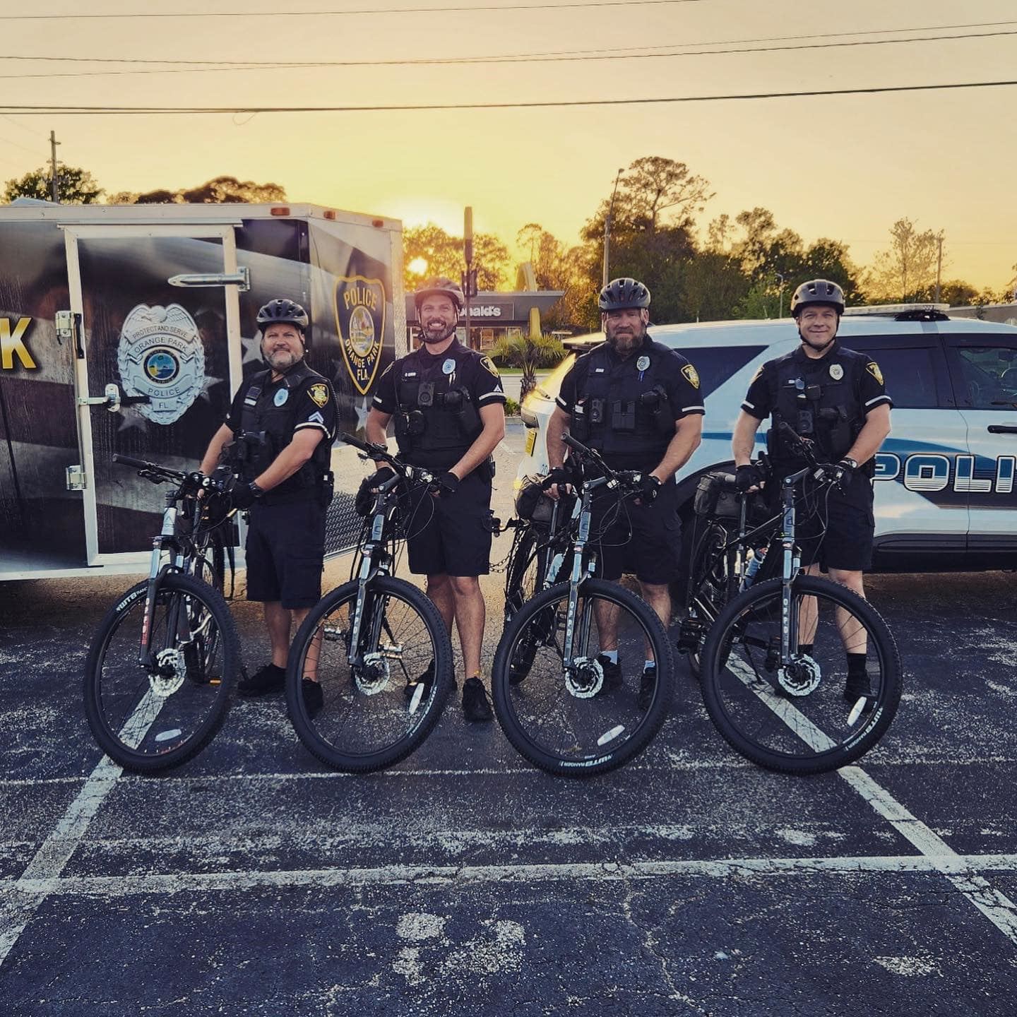 4 police officers on bikes in a parking lot with SUV police vehicle and police trailer in background