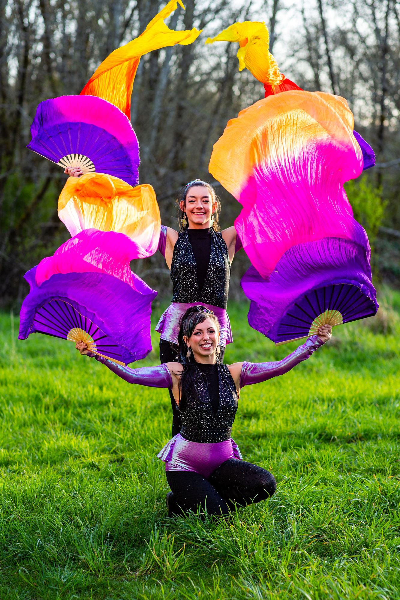 Two women, one standing, one sitting on the ground, with bright scarves billowing in the air