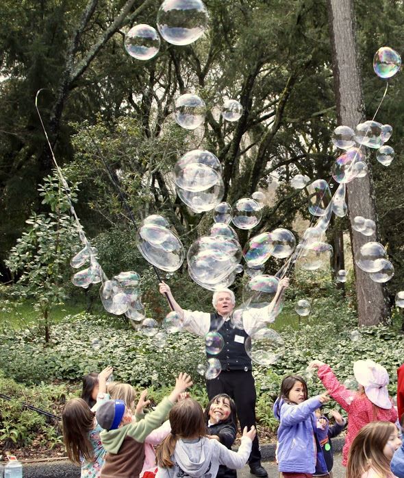 Photo: an outdoor scene filled with children reaching for bubles created by performer