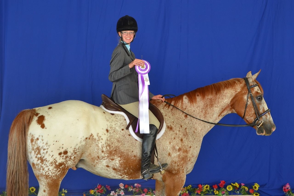4-H exhibitor on her appaloosa horse holding a ribbon