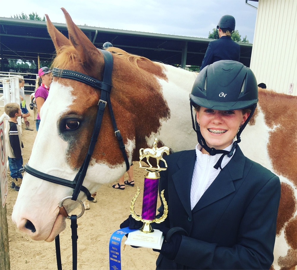 A 4-H girl standing next to her horse holding a trophy smiling