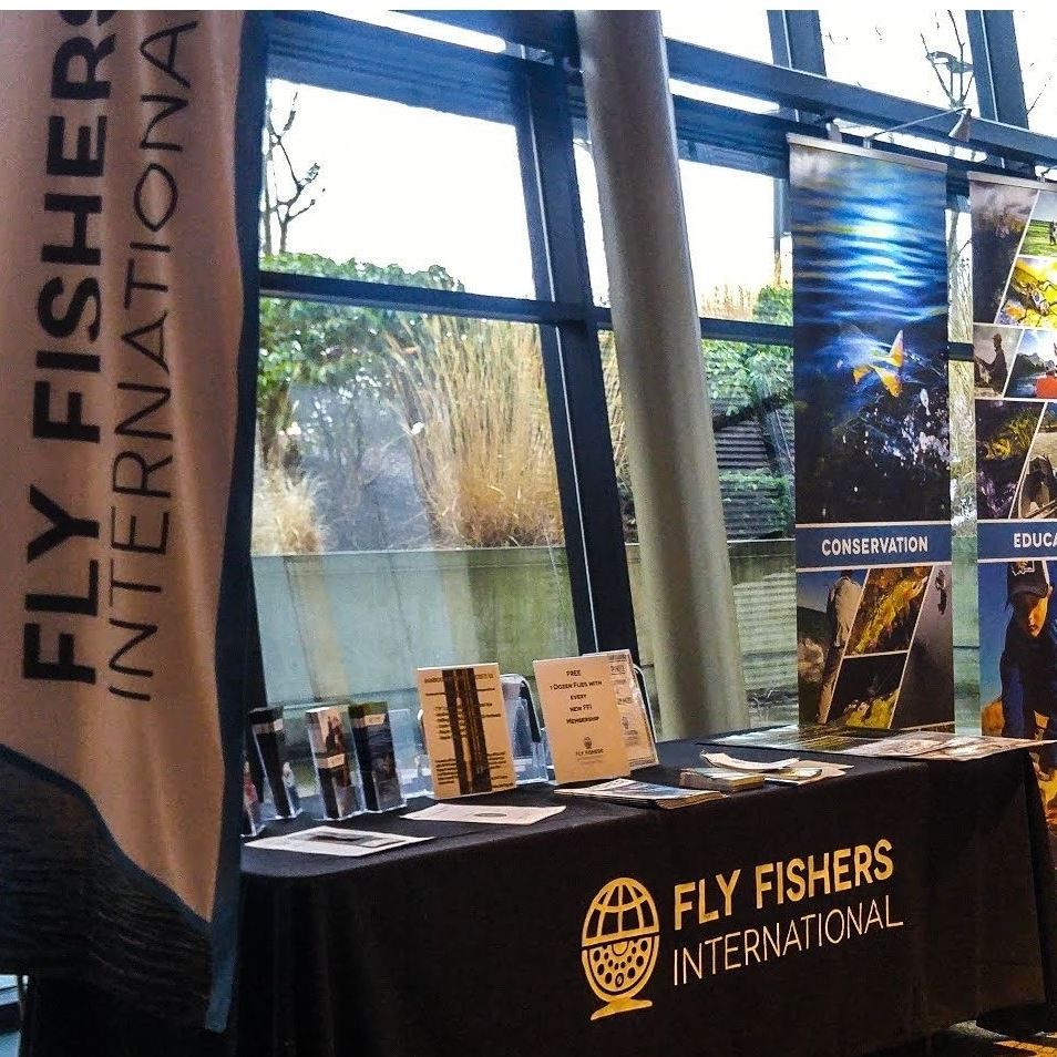 A booth is set against a large window. The booth contains flyers, brochures and banners advertising a fly fishing group.
