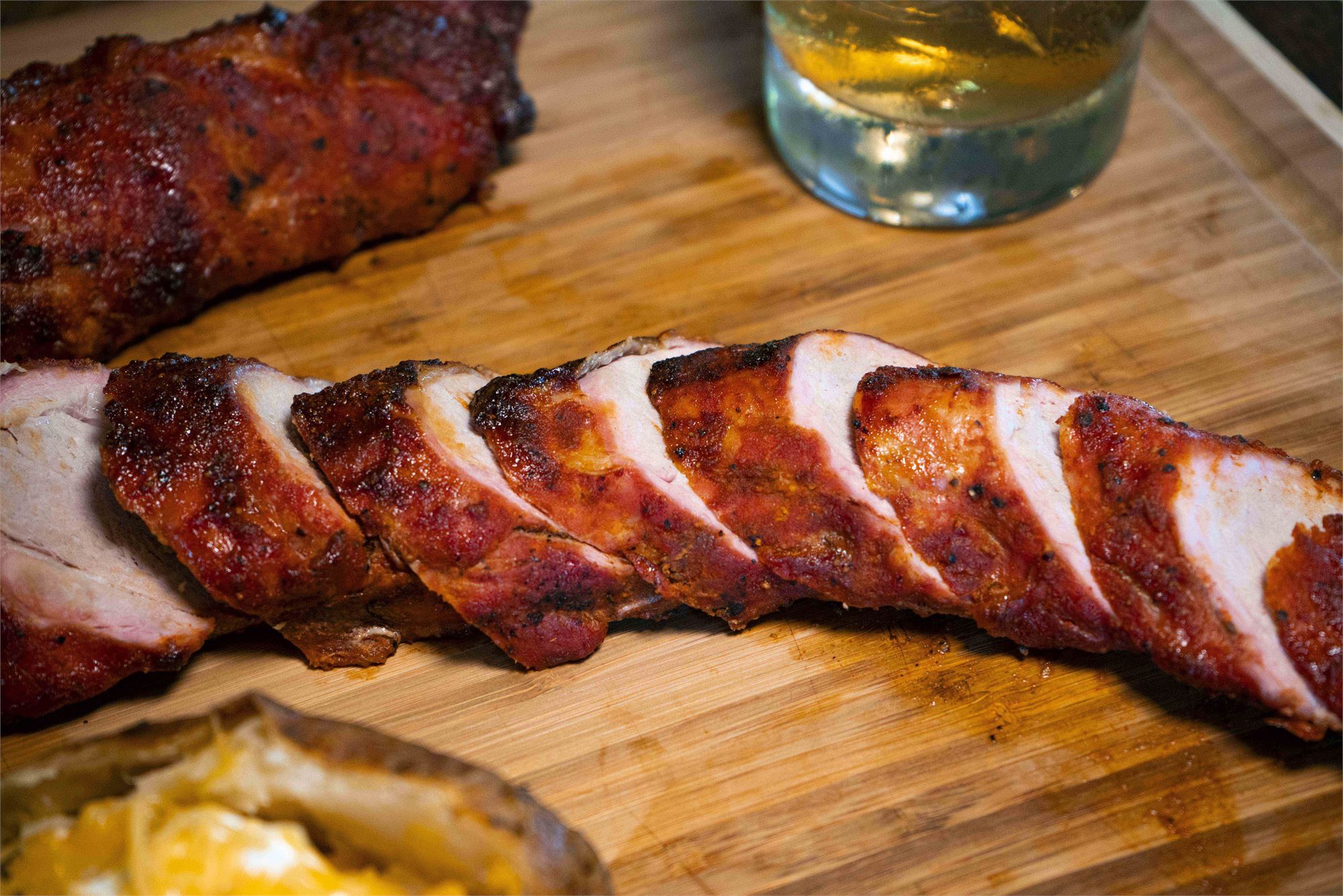 Sliced pork tenderloin laid out on a wooden cutting board with a glass of whiskey