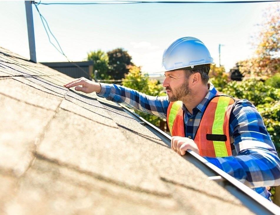 Man in hard hat with vest inspecting a roof.