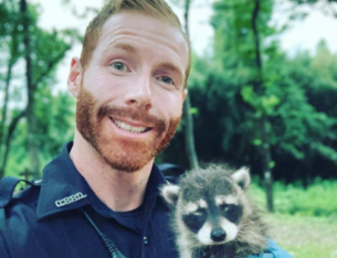Police officer holding a baby racoon. 