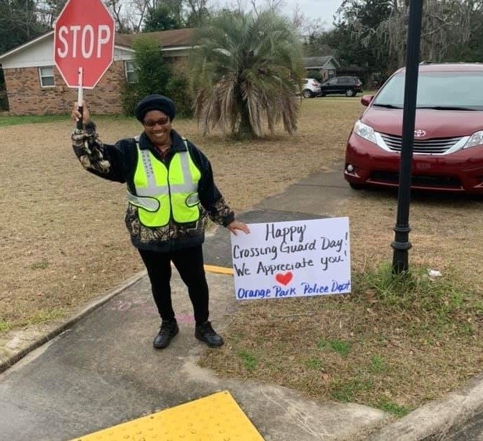 Photo of a crossing guard, a black woman, holding a stop sign at an intersection