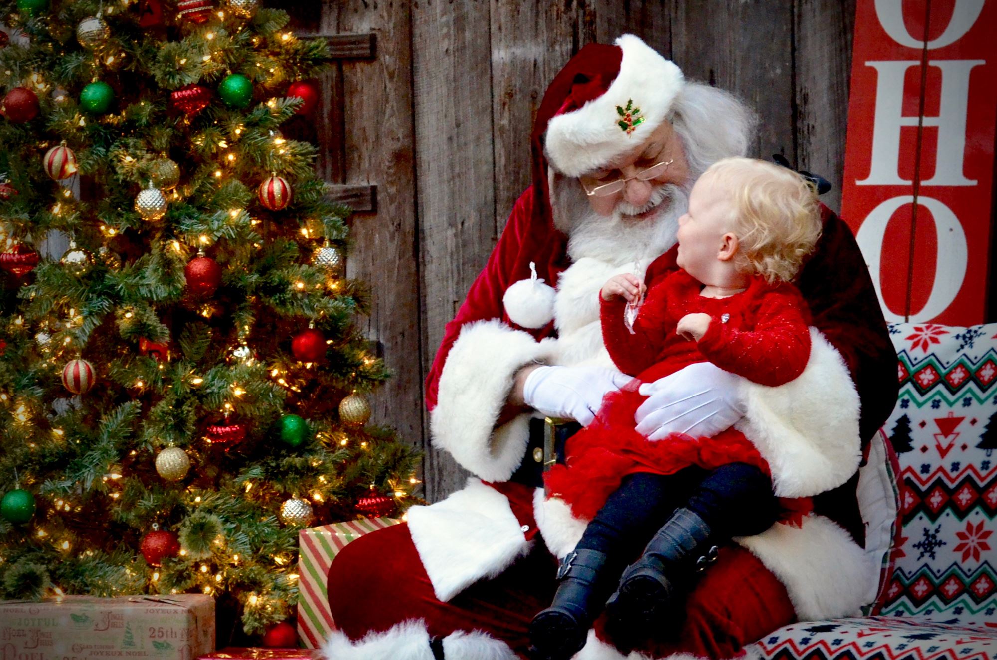 Santa Claus with a small child on his lap. Christmas tree in background.
