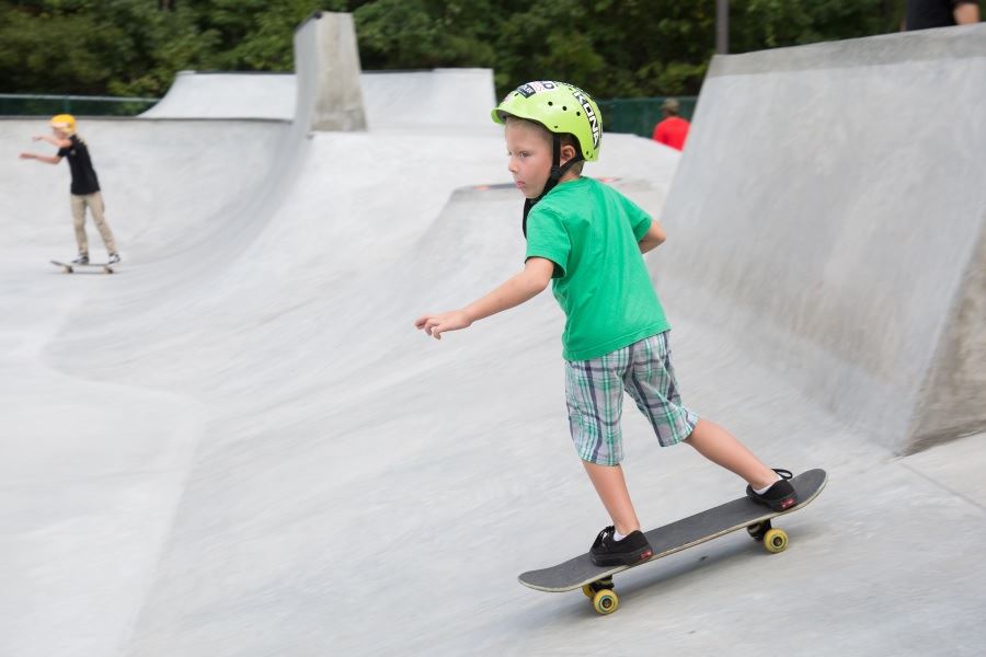 child in green shirt on concrete skateboard ramp additional child in background