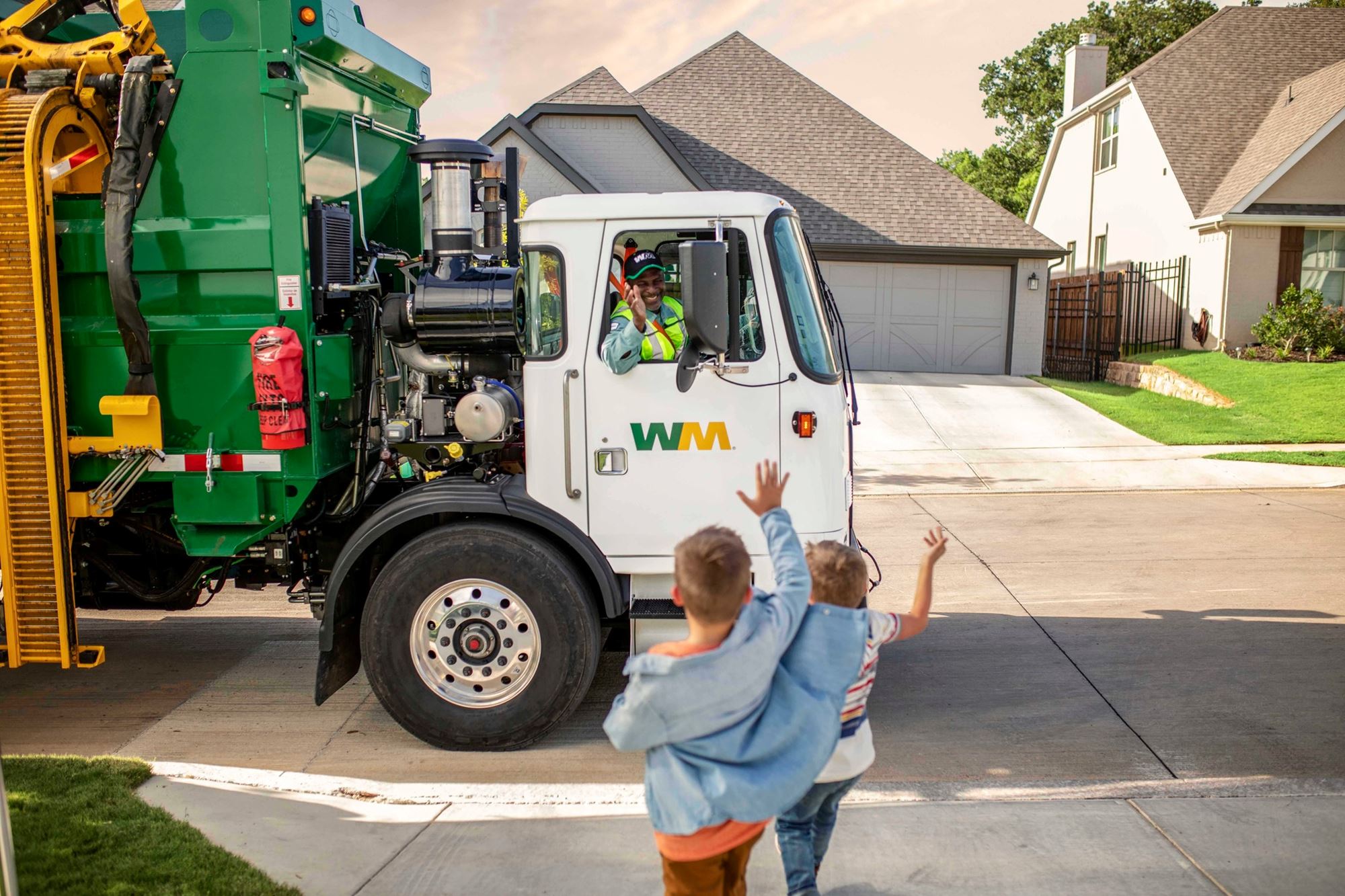2 children waving at a Waste Management garbage truck .