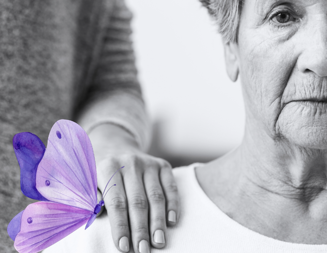 black and white photo of an older woman seated and someone's hand on her shoulder with a purple butterfly.