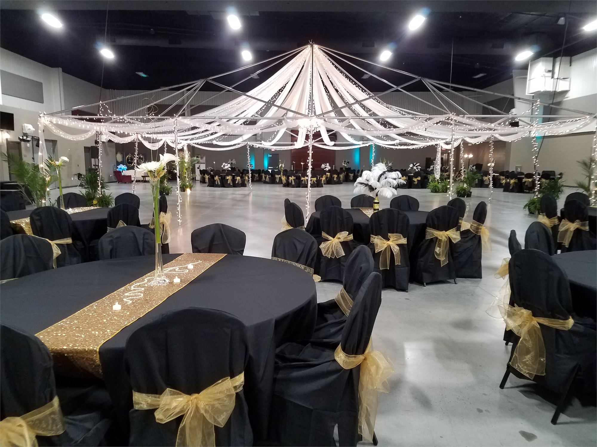 Indoor Expo Hall decorated for the Taylor Prom. Tables covered in black table clothes and a canopy with lights over the dance floor